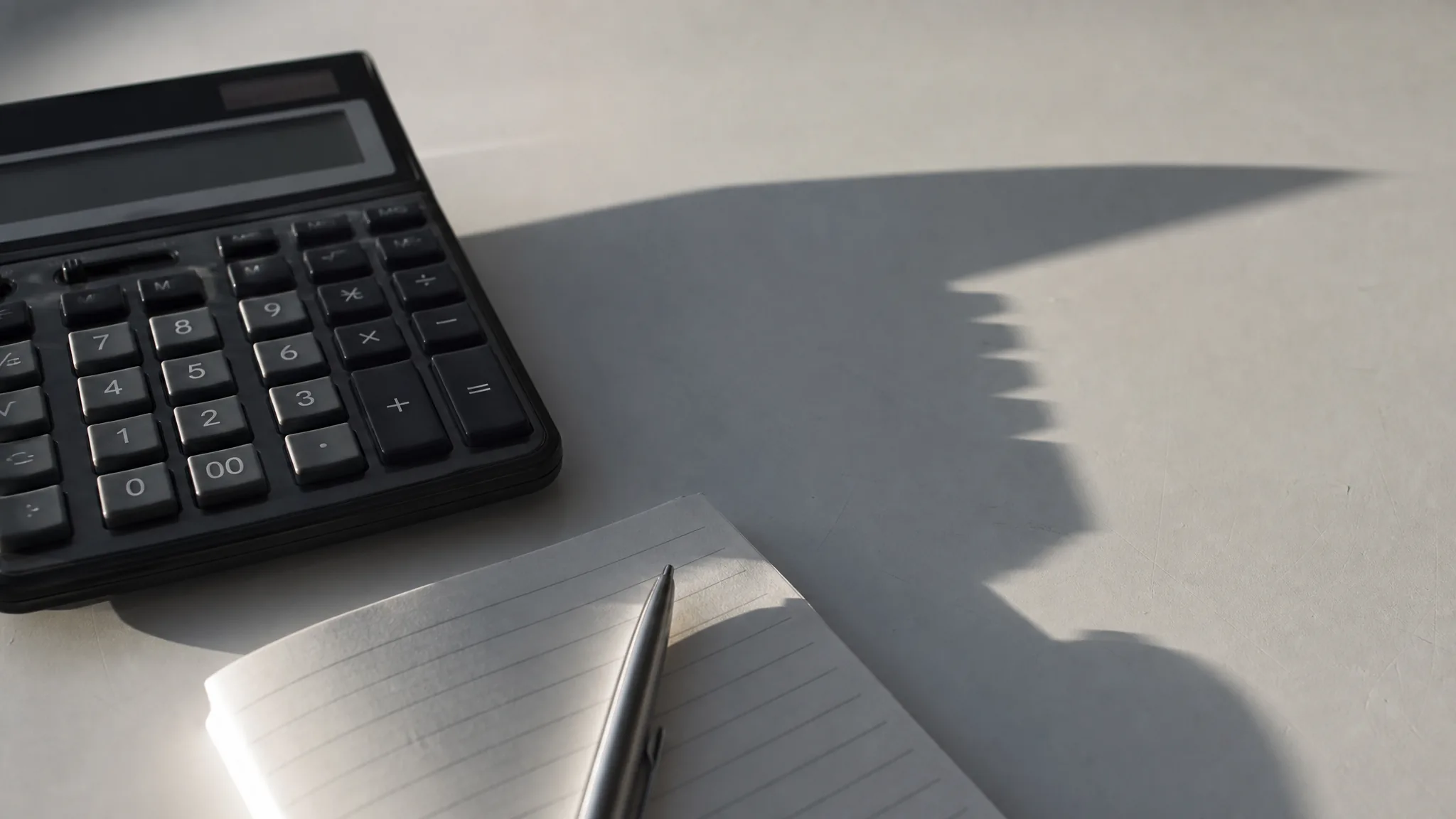 A desk calculator and notepad in strong morning light